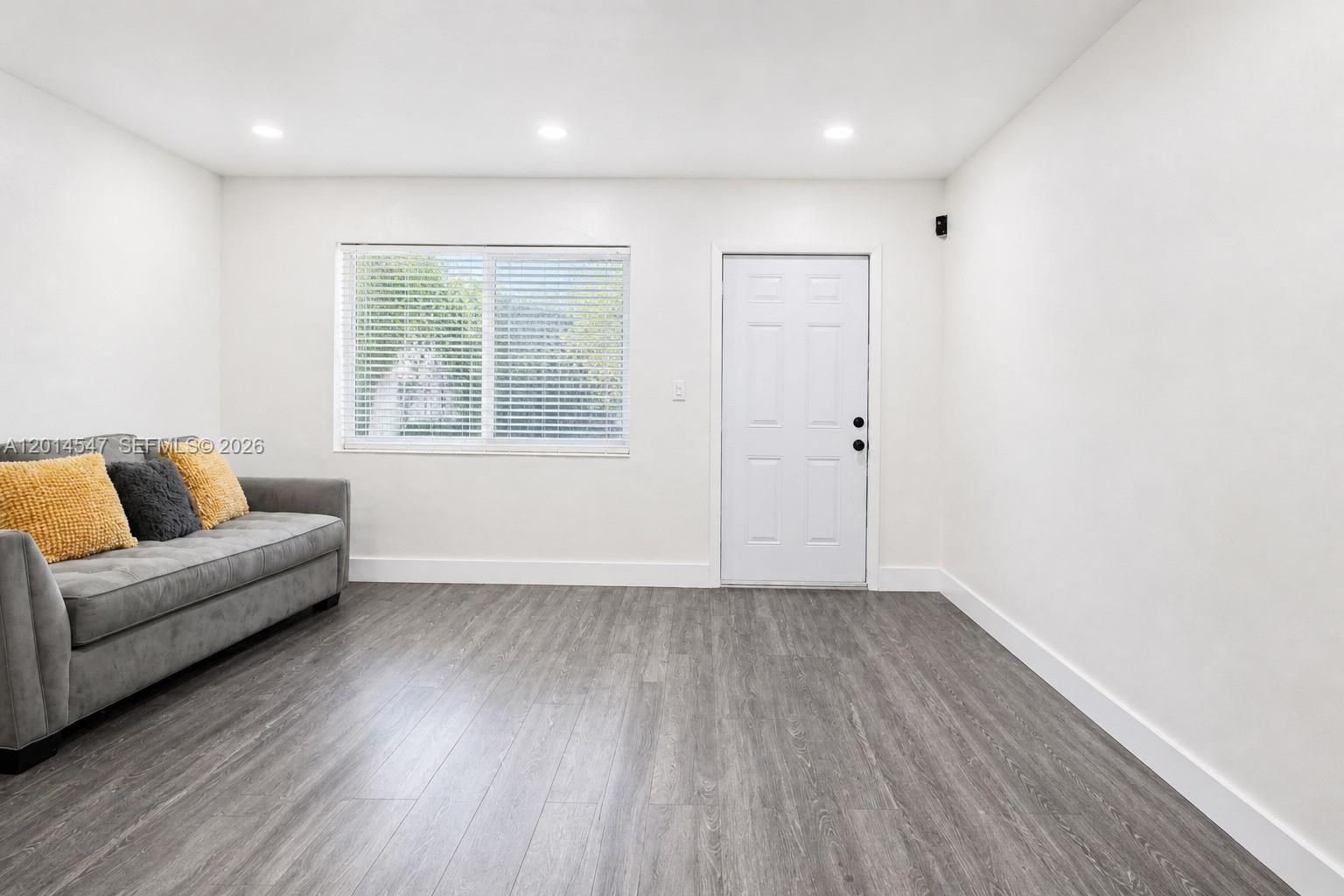 A living room features gray wood-look flooring, white walls, a gray sofa, and a white door — 1631 NW 114th St, Miami FL 33167, MIAMI, FL