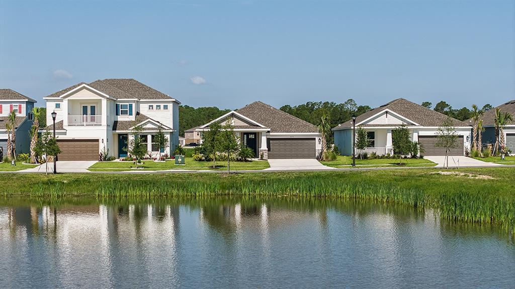 A row of suburban houses sits behind a pond under a clear blue sky — 5435 CROWN POINT ROAD, KISSIMMEE, FL