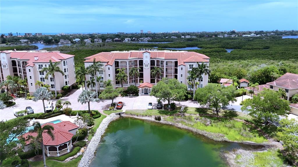 An aerial view shows a multi-story apartment building with a pool and a pond — 5420 EAGLES POINT CIRCLE UNIT 206, SARASOTA, FL