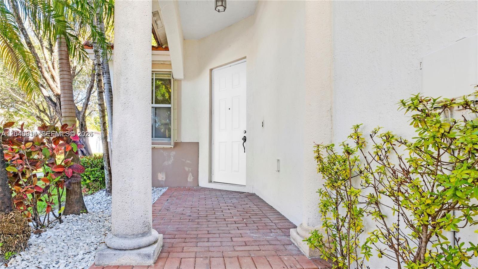 A white front door is centered on a brick porch between two concrete columns — 10863 NW 85th St # 0, Doral FL 33178, DORAL, FL