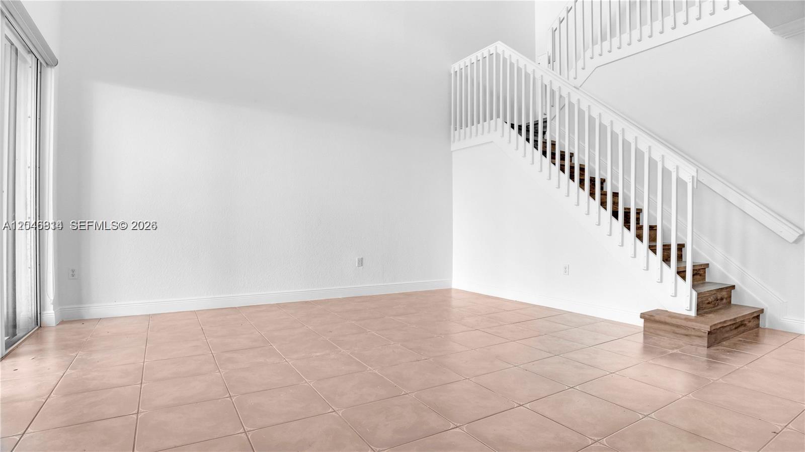 An empty room features white walls, tile flooring, and a staircase with white railings — 10863 NW 85th St # 0, Doral FL 33178, DORAL, FL
