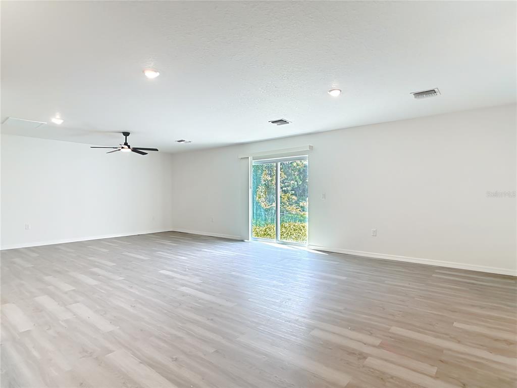 A spacious, empty room features light-colored wood-look flooring, white walls, and a sliding glass door — 3067 QUARTER STREET, NORTH PORT, FL