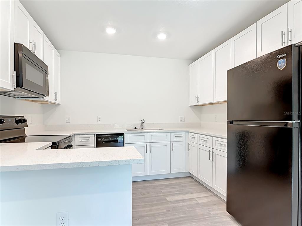 A kitchen features white cabinets, light countertops, a black refrigerator, and a black microwave — 3067 QUARTER STREET, NORTH PORT, FL