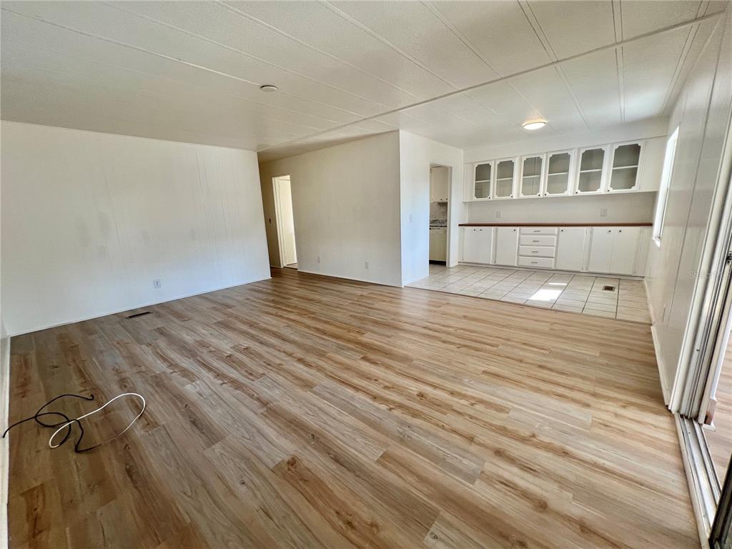 An open-concept living area features light wood-look flooring and an adjacent kitchen with white cabinetry — 222 HAWTHORNE BOULEVARD, LEESBURG, FL