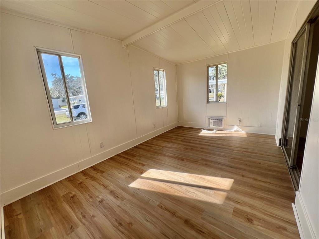 An empty room features light wood-look flooring, white paneled walls, and two windows — 222 HAWTHORNE BOULEVARD, LEESBURG, FL