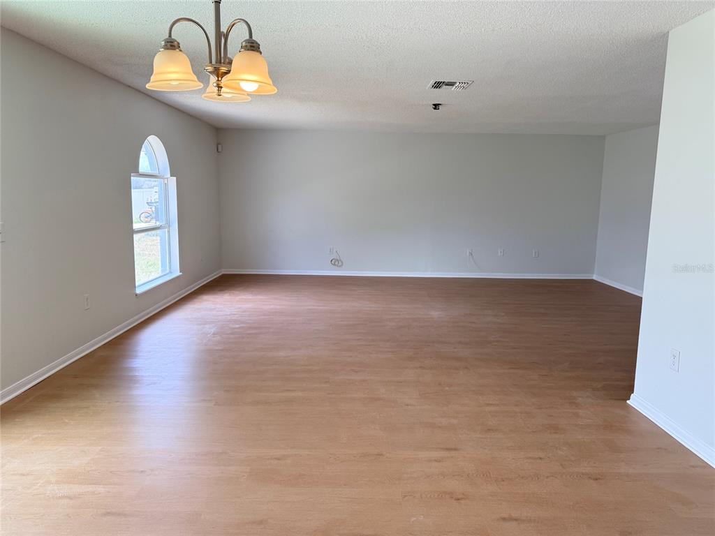 An empty room with light wood-look flooring, a chandelier, and an arched window — 5871 WINDRIDGE DRIVE, WINTER HAVEN, FL