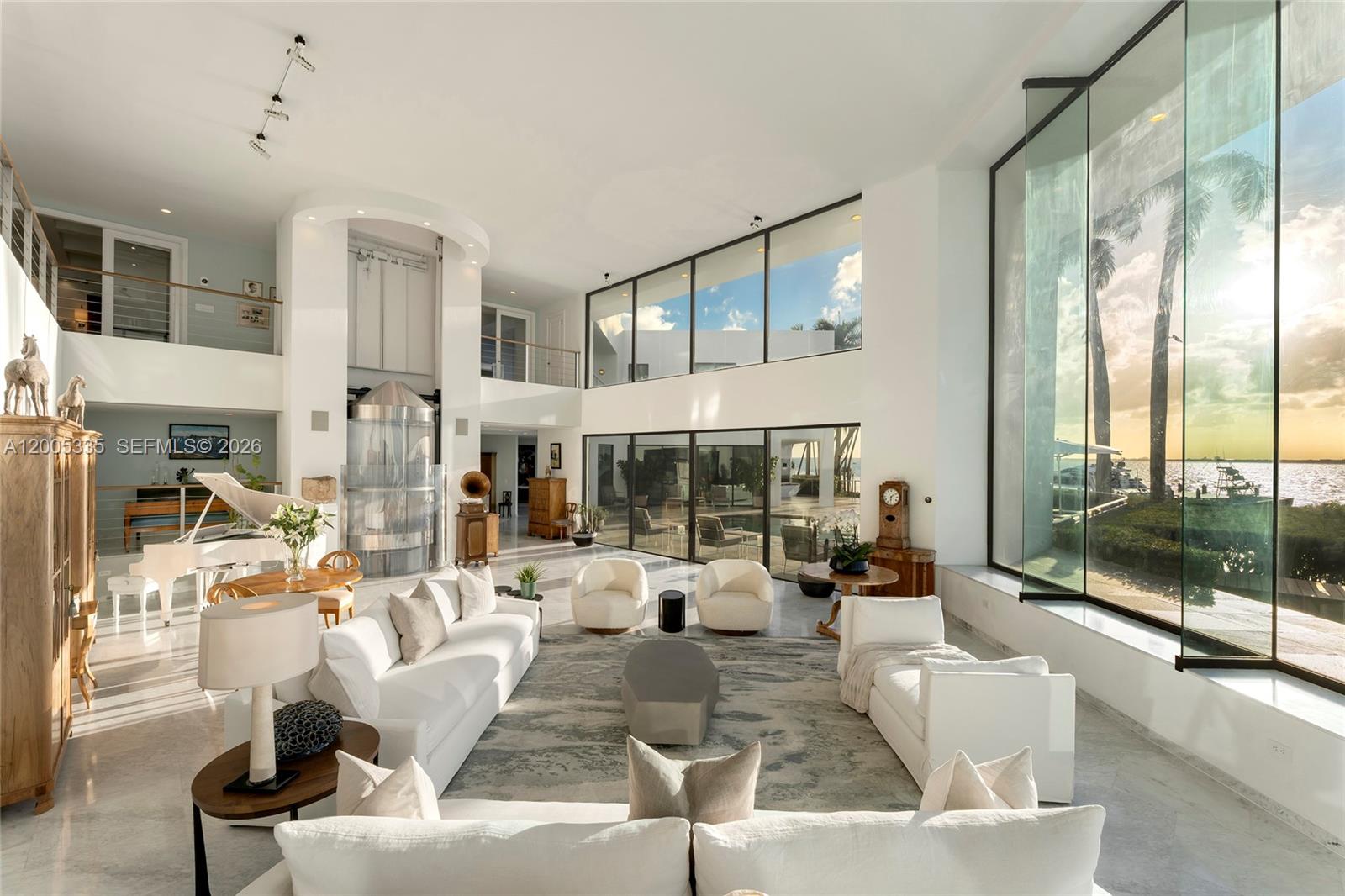 A spacious living room features white furniture, a grand piano, and floor-to-ceiling windows overlooking water — 485 W Matheson Dr, Key Biscayne FL 33149, KEY BISCAYNE, FL