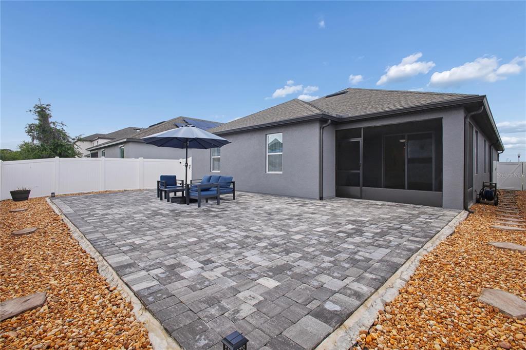 A backyard features a large paver patio, a screened-in porch, and a white vinyl fence — 5732 IRON BRAND ROAD, ST CLOUD, FL