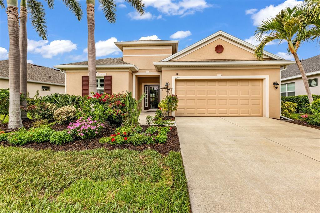 A single-story house with a tan stucco exterior, a two-car garage, and a landscaped yard — 2205 TERRACINA DRIVE, VENICE, FL