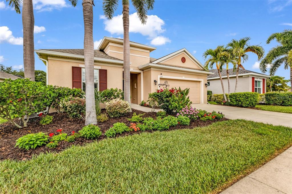 A single-story tan house with a two-car garage, palm trees, and landscaped front yard — 2205 TERRACINA DRIVE, VENICE, FL