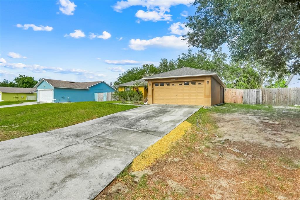 A tan house with a two-car garage and a concrete driveway under a blue sky — 10752 CRESCENDO LOOP, CLERMONT, FL