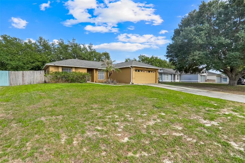 A single-story tan house with a two-car garage and a large front lawn — 10752 CRESCENDO LOOP, CLERMONT, FL