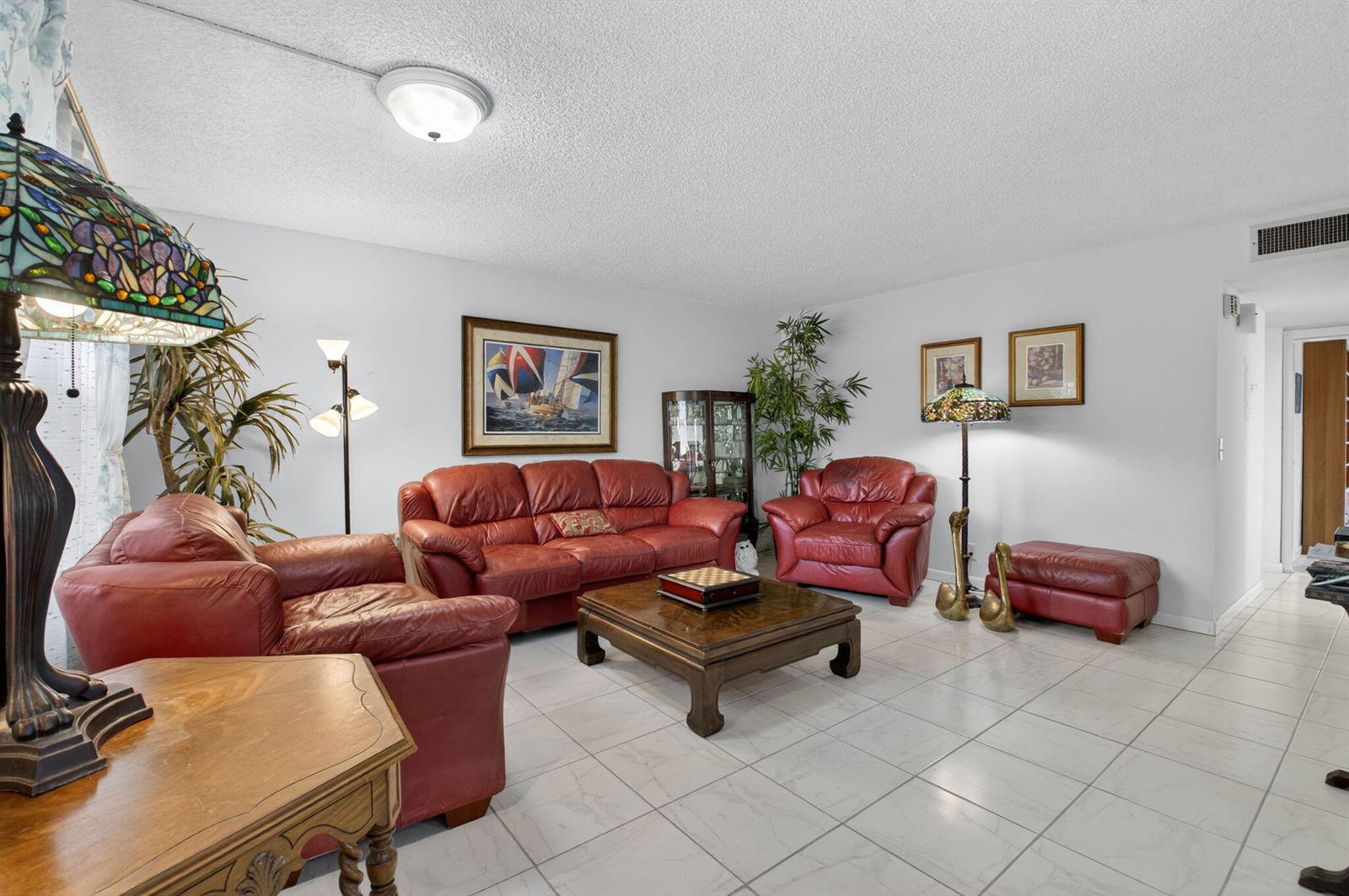 A living room features red leather furniture, a wooden coffee table, and white tile flooring — 502 Normandy K, Delray Beach FL 33484, DELRAY BEACH, FL