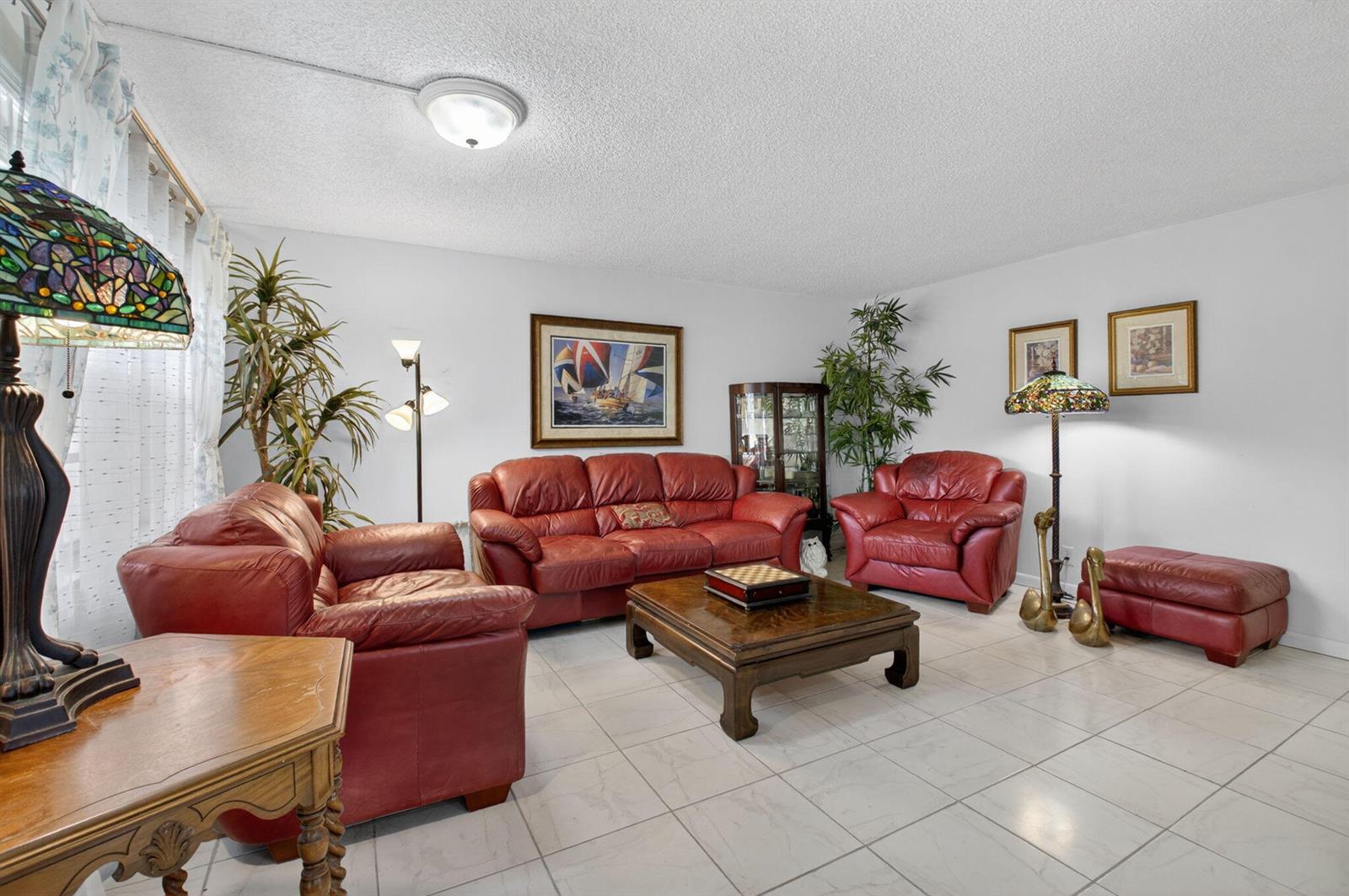 A living room features red leather furniture, a wooden coffee table, and tiled flooring — 502 Normandy K, Delray Beach FL 33484, DELRAY BEACH, FL