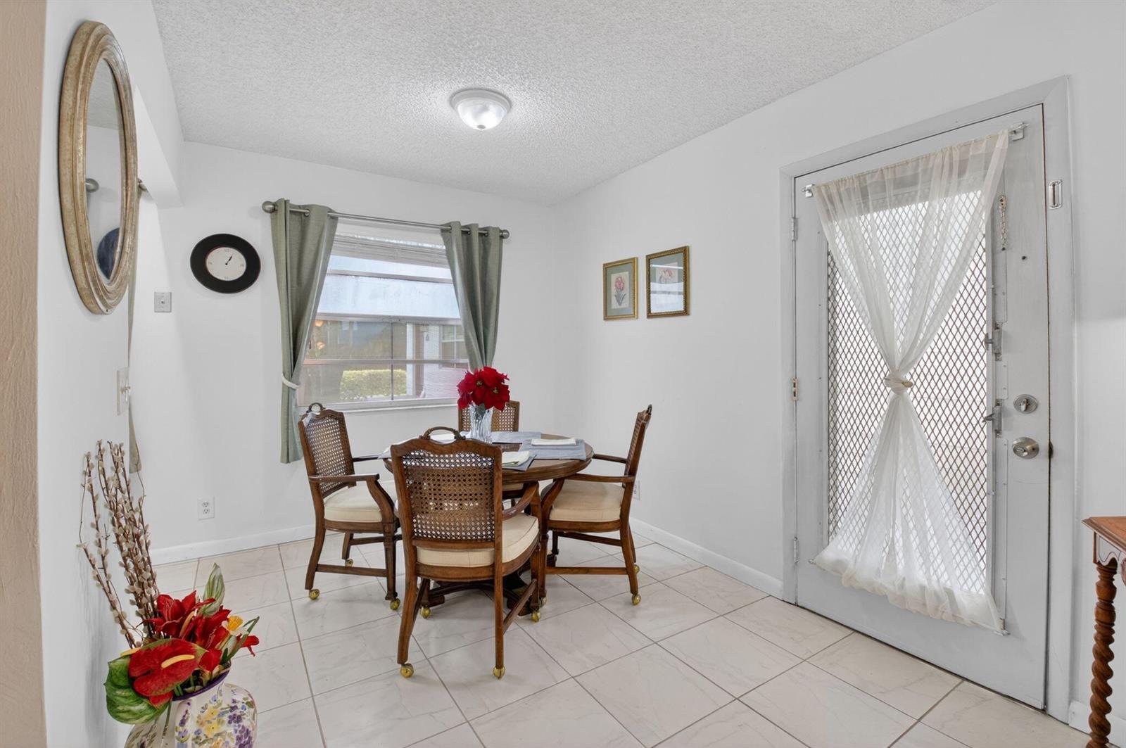 A dining area features a round wooden table with four chairs, tiled floors, and a door — 502 Normandy K, Delray Beach FL 33484, DELRAY BEACH, FL