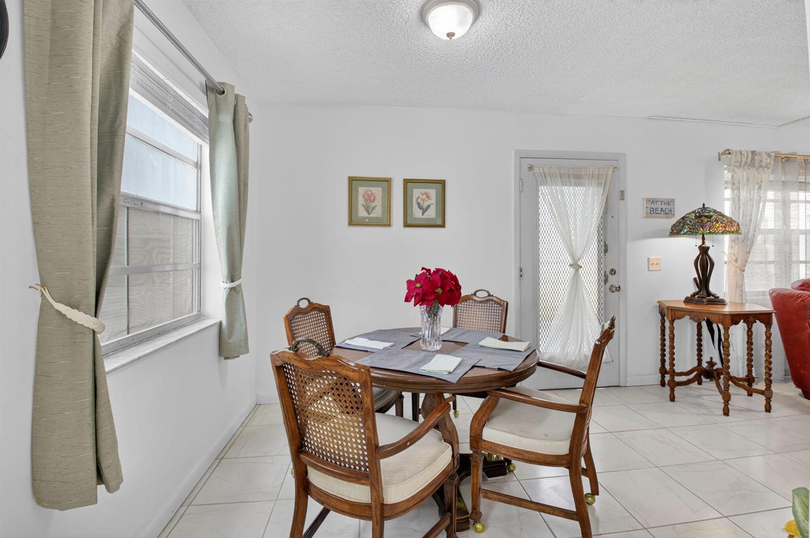 A dining area features a round wooden table with four cane-back chairs on tiled flooring — 502 Normandy K, Delray Beach FL 33484, DELRAY BEACH, FL