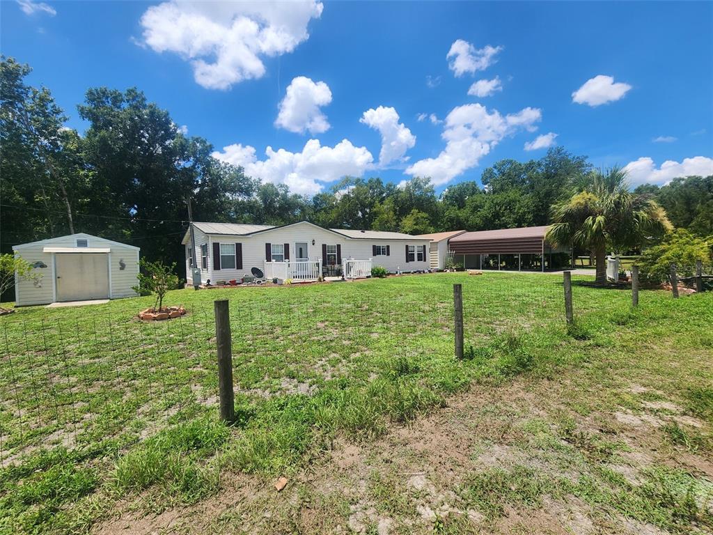 A single-story house with a shed and a carport sits on a grassy fenced lot — 12398 SW CRENSHAW AVENUE, ARCADIA, FL