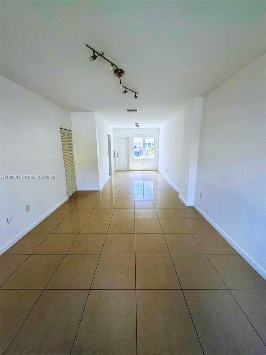 An empty room features light-colored walls, large beige floor tiles, and a track lighting fixture — 440 NW 84th Ter # 440, Miami FL 33150, MIAMI, FL