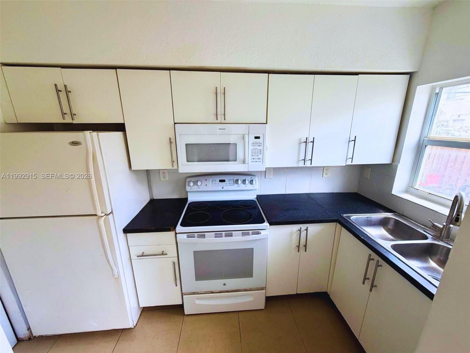 A kitchen features white cabinets, black countertops, a white refrigerator, and a white stove — 440 NW 84th Ter # 440, Miami FL 33150, MIAMI, FL