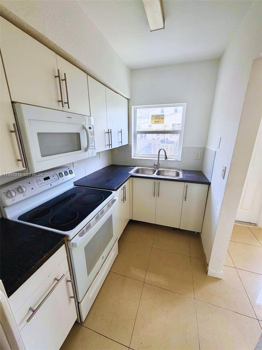 A small kitchen features white cabinets, black countertops, a white stove, and a window — 440 NW 84th Ter # 440, Miami FL 33150, MIAMI, FL
