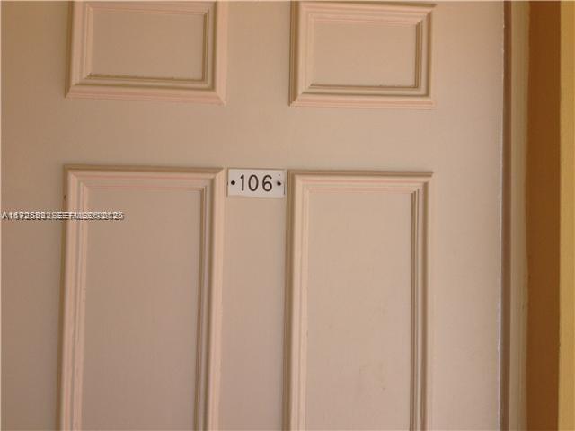 A beige door with a rectangular panel design features a small sign labeled 106 — 241 SE 9th Ave # 106, Pompano Beach FL 33060, POMPANO BEACH, FL