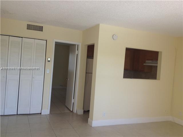 A room with light-colored walls, tile floors, louvered closet doors, and a kitchen pass-through window — 241 SE 9th Ave # 106, Pompano Beach FL 33060, POMPANO BEACH, FL