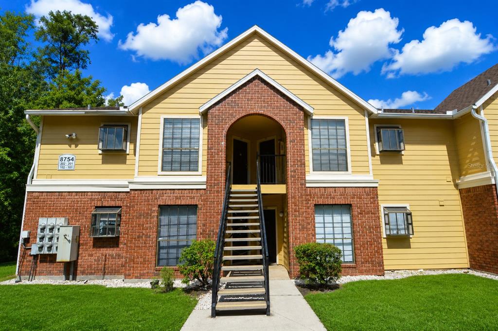 A two-story apartment building features yellow siding, brick accents, and a central exterior staircase — 8754 MALLARD RESERVE DRIVE UNIT 202, TAMPA, FL