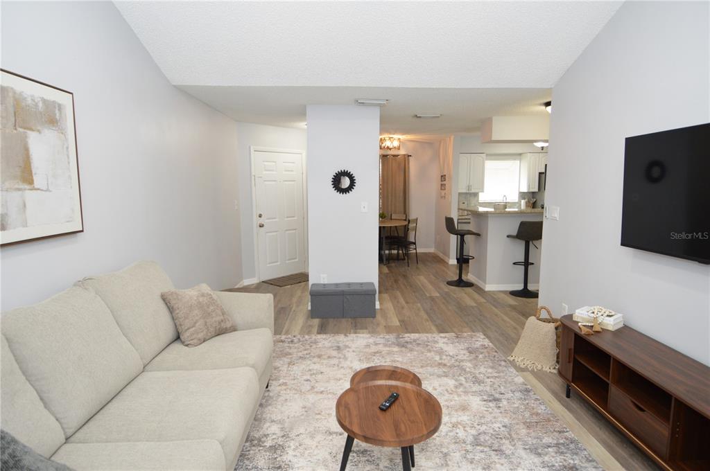 A living room with a beige sofa, wood-look flooring, and an open view to the kitchen — 8754 MALLARD RESERVE DRIVE UNIT 202, TAMPA, FL