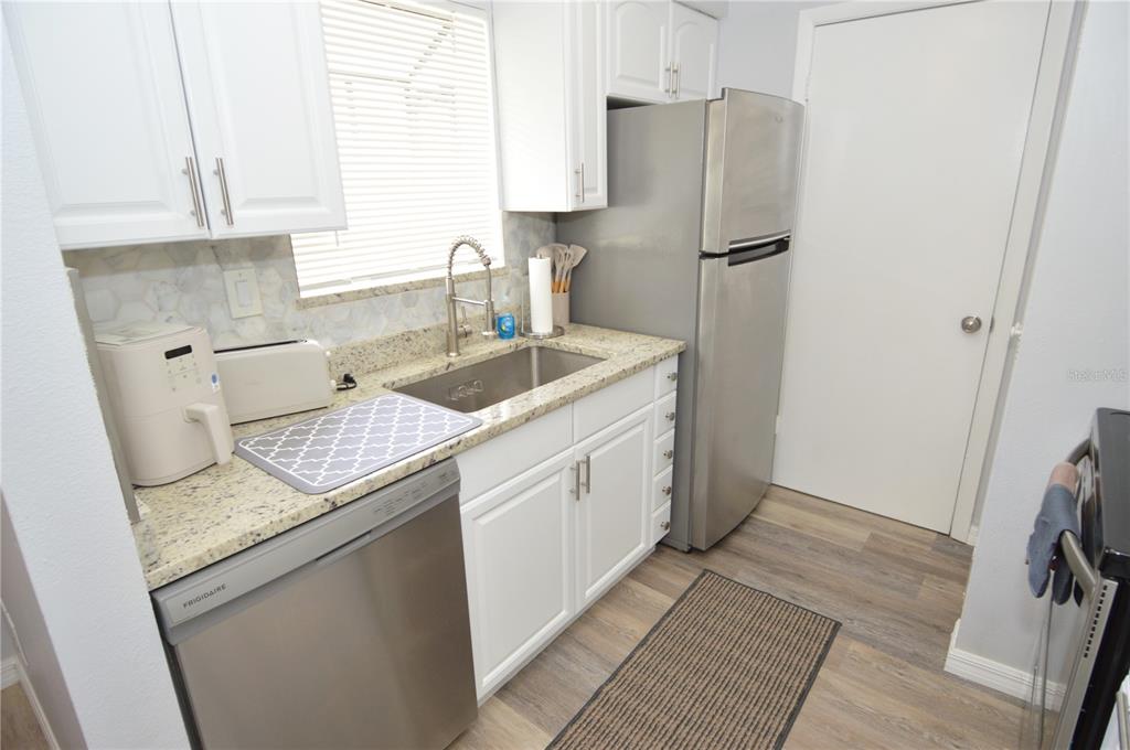 A kitchen features white cabinets, granite countertops, stainless steel appliances, and wood-look flooring — 8754 MALLARD RESERVE DRIVE UNIT 202, TAMPA, FL