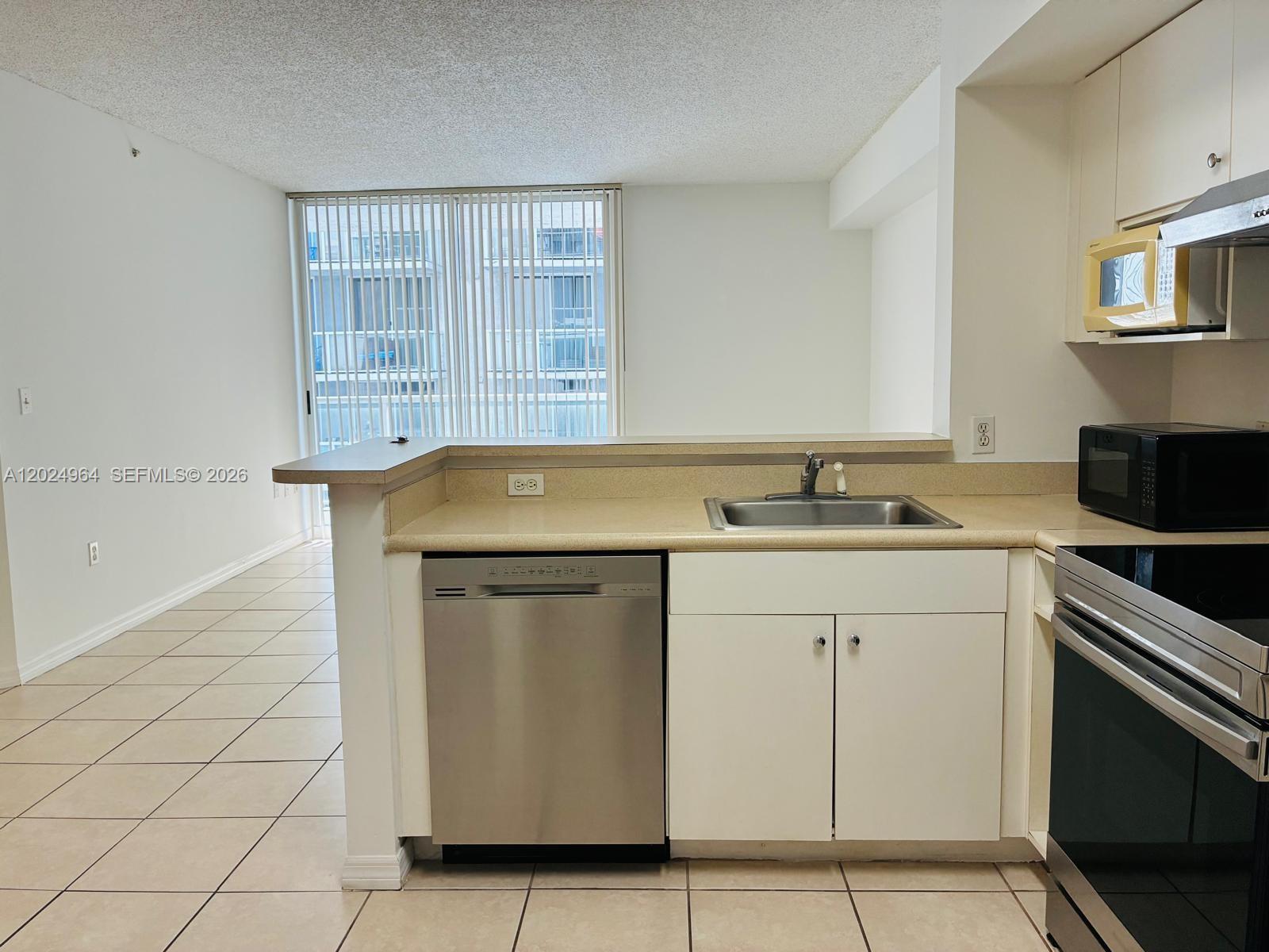 A kitchen with white cabinets, stainless steel appliances, and a pass-through counter overlooking a room — 5085 NW 7th St # 909, Miami FL 33126, MIAMI, FL