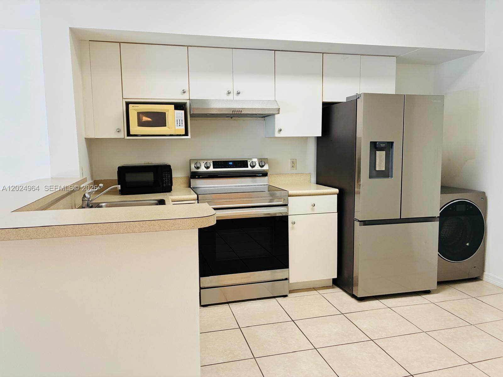 A kitchen features white cabinets, stainless steel appliances, a beige countertop, and tiled flooring — 5085 NW 7th St # 909, Miami FL 33126, MIAMI, FL