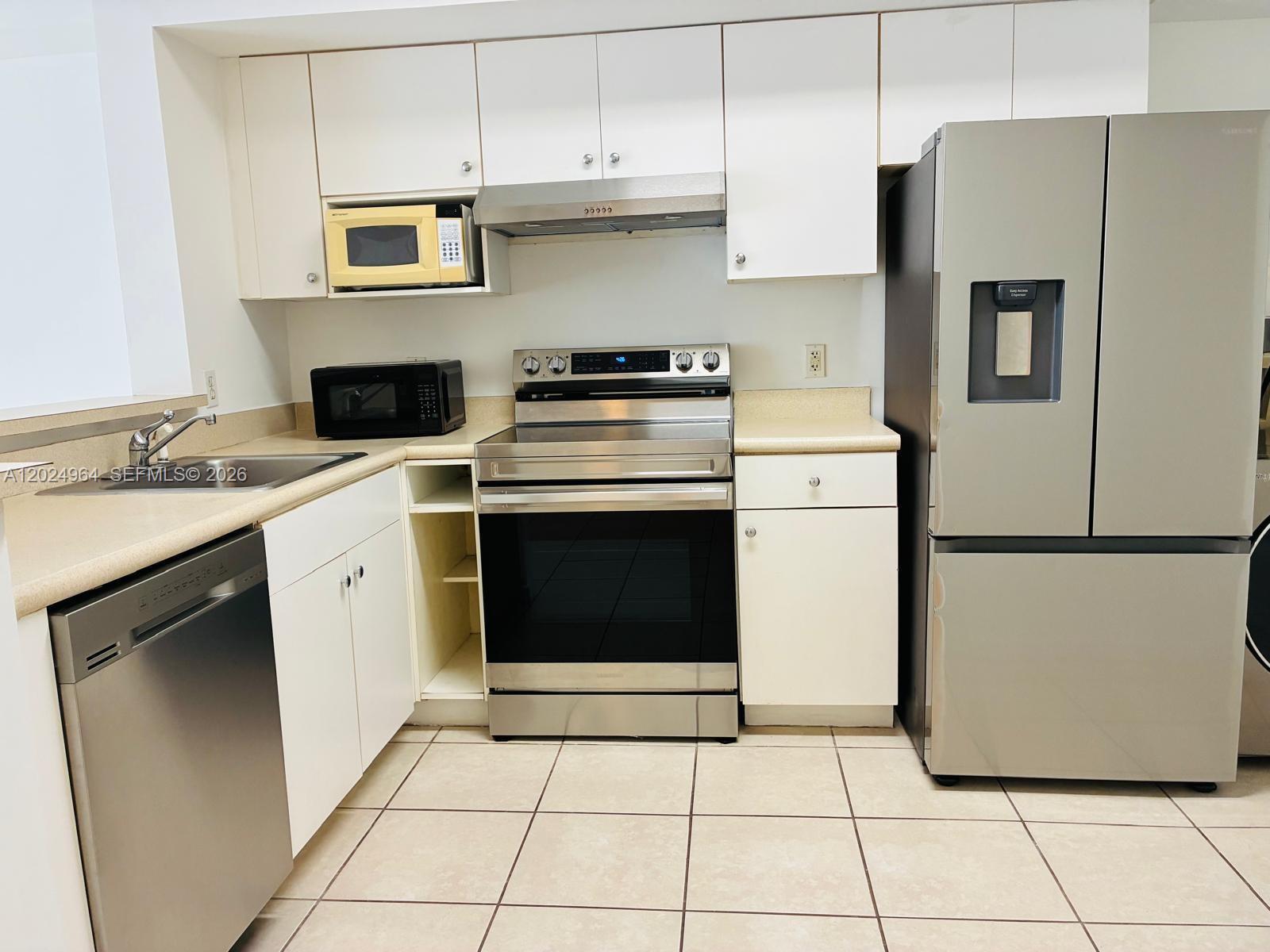 A kitchen featuring white cabinets, stainless steel appliances, beige countertops, and light-colored tile flooring — 5085 NW 7th St # 909, Miami FL 33126, MIAMI, FL