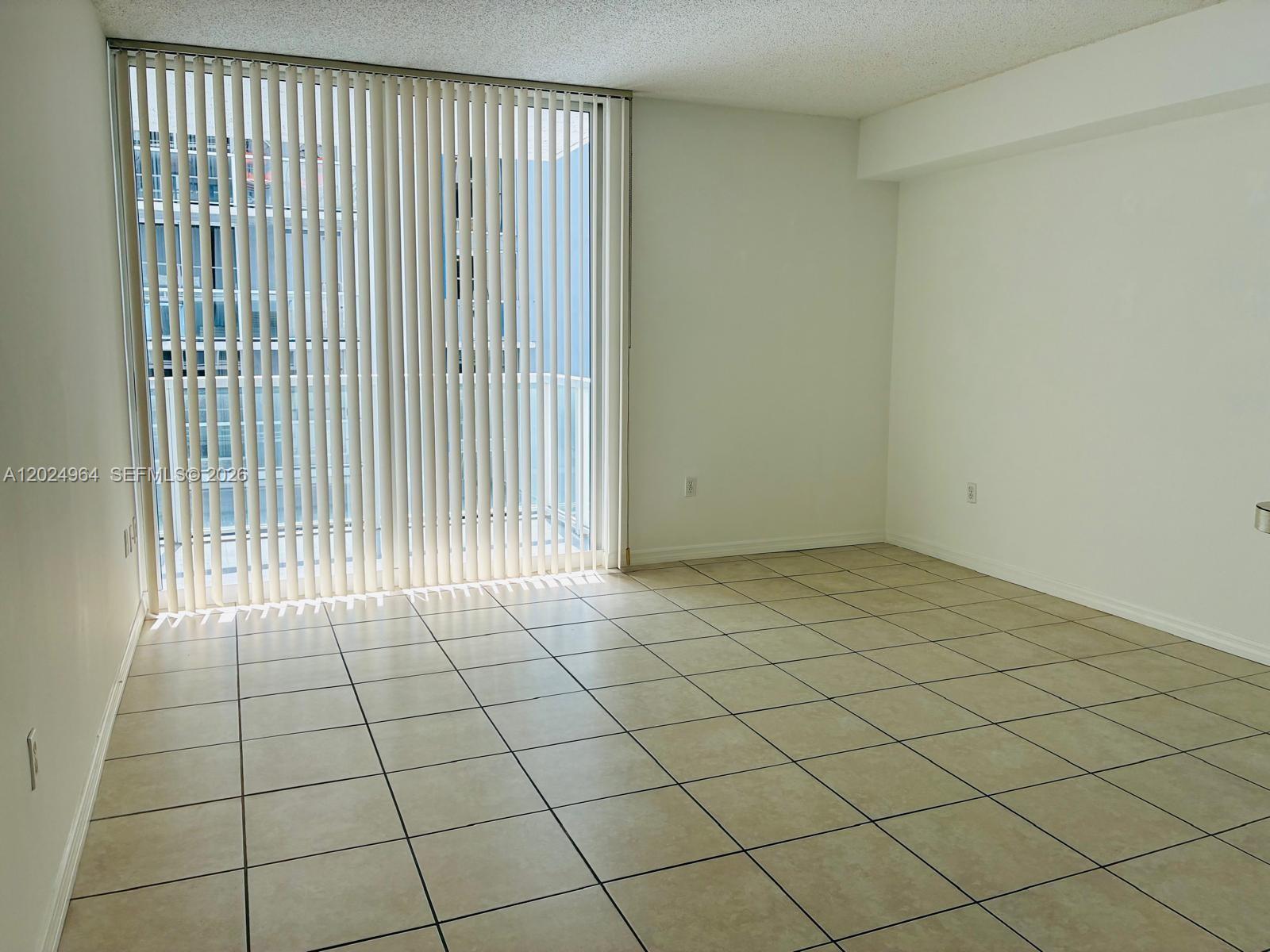 An empty room features light-colored tile flooring, white walls, and vertical blinds covering a balcony door — 5085 NW 7th St # 909, Miami FL 33126, MIAMI, FL
