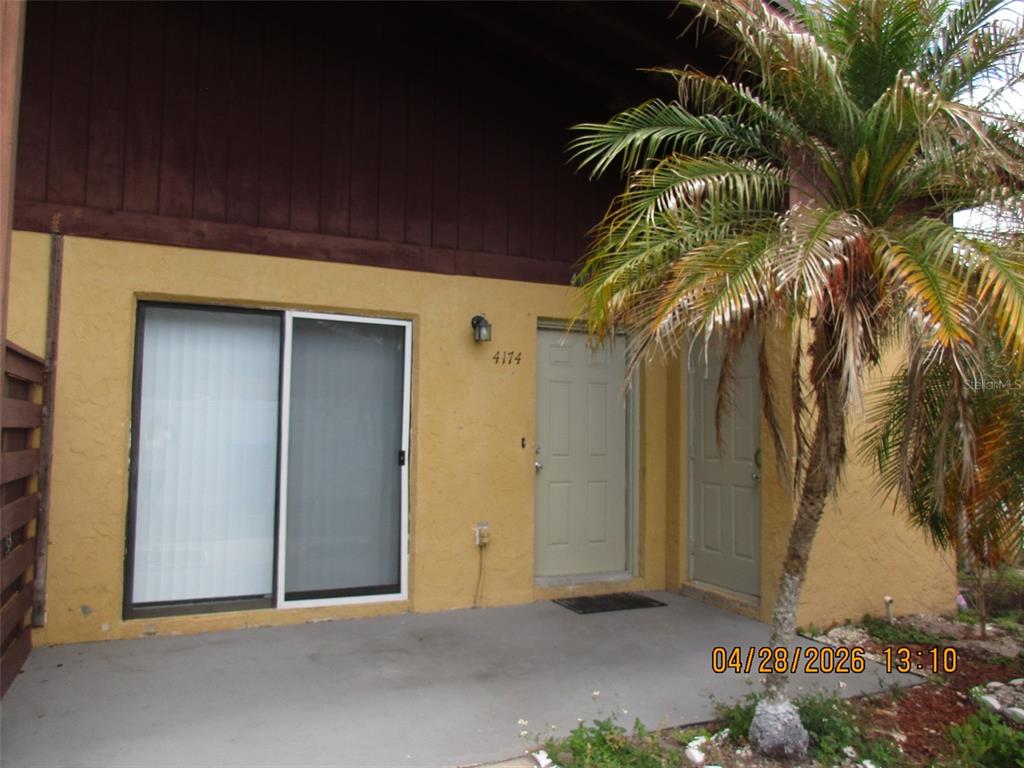 A yellow stucco building exterior features a sliding glass door, a front door, and palm tree — 4174 CORSAIR AVENUE UNIT 4174, KISSIMMEE, FL