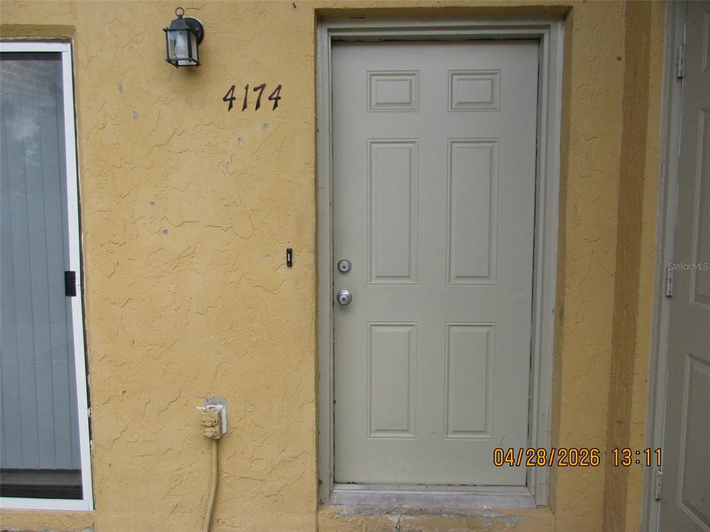 A beige exterior wall features a six-panel door, a house number, and a light fixture — 4174 CORSAIR AVENUE UNIT 4174, KISSIMMEE, FL
