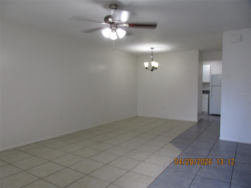 An empty room features light-colored tile flooring, a ceiling fan, and a hanging light fixture — 4174 CORSAIR AVENUE UNIT 4174, KISSIMMEE, FL