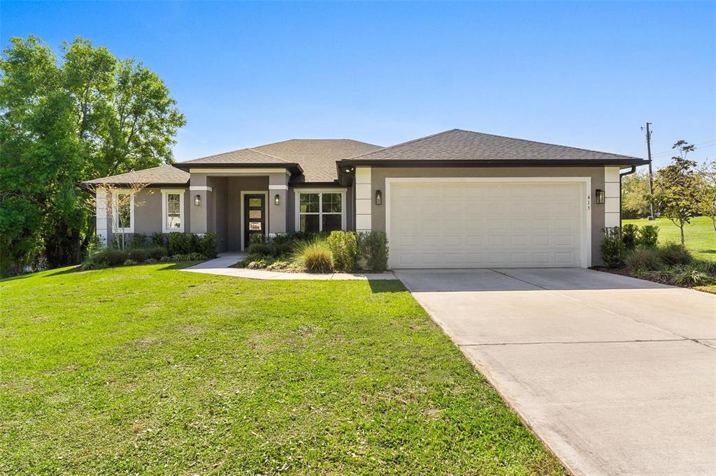 A single-story house with a gray stucco exterior, a two-car garage, and a front lawn — 415 N DIXIE DRIVE, HOWEY IN THE HILLS, FL