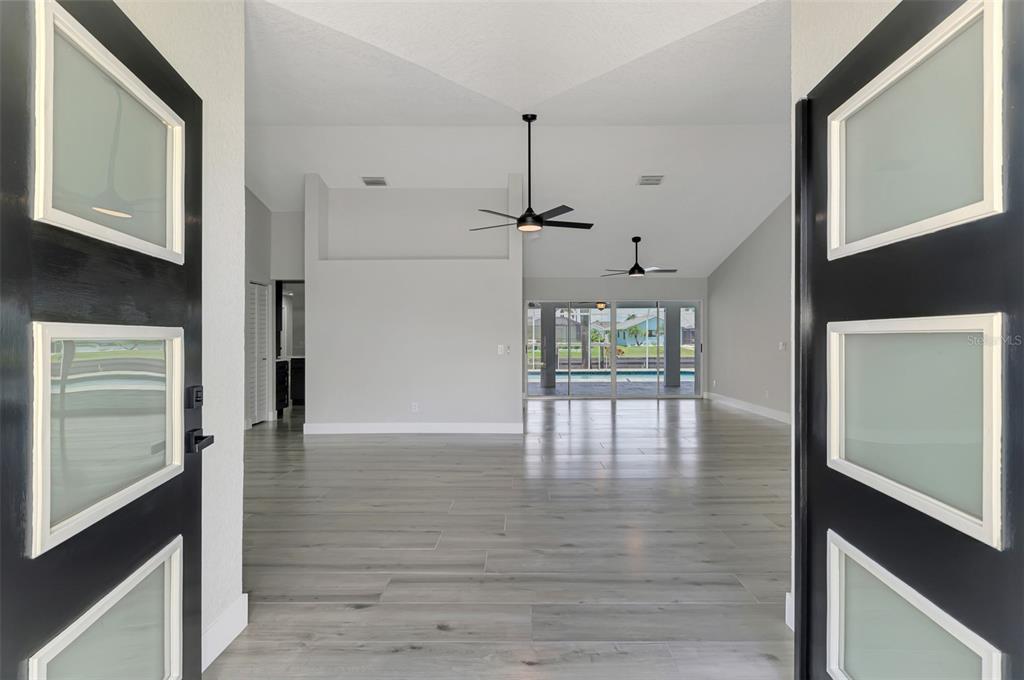 An open-concept living area with light wood-look flooring, vaulted ceilings, and sliding glass patio doors — 3077 STONE STREET, PORT CHARLOTTE, FL