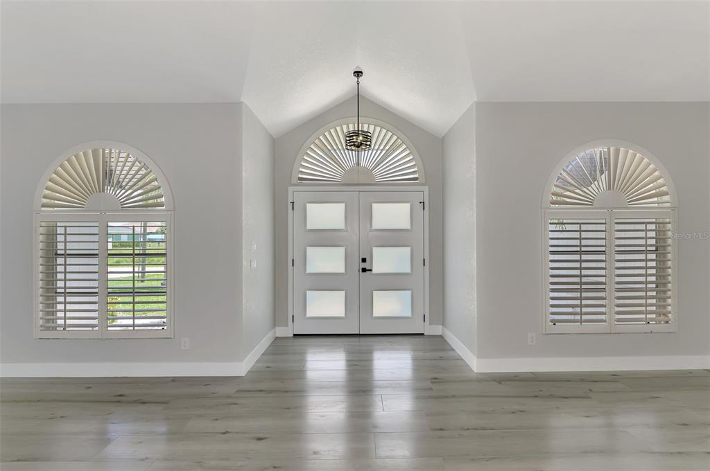A bright entryway features light wood-look flooring, double doors with frosted glass, and arched windows — 3077 STONE STREET, PORT CHARLOTTE, FL