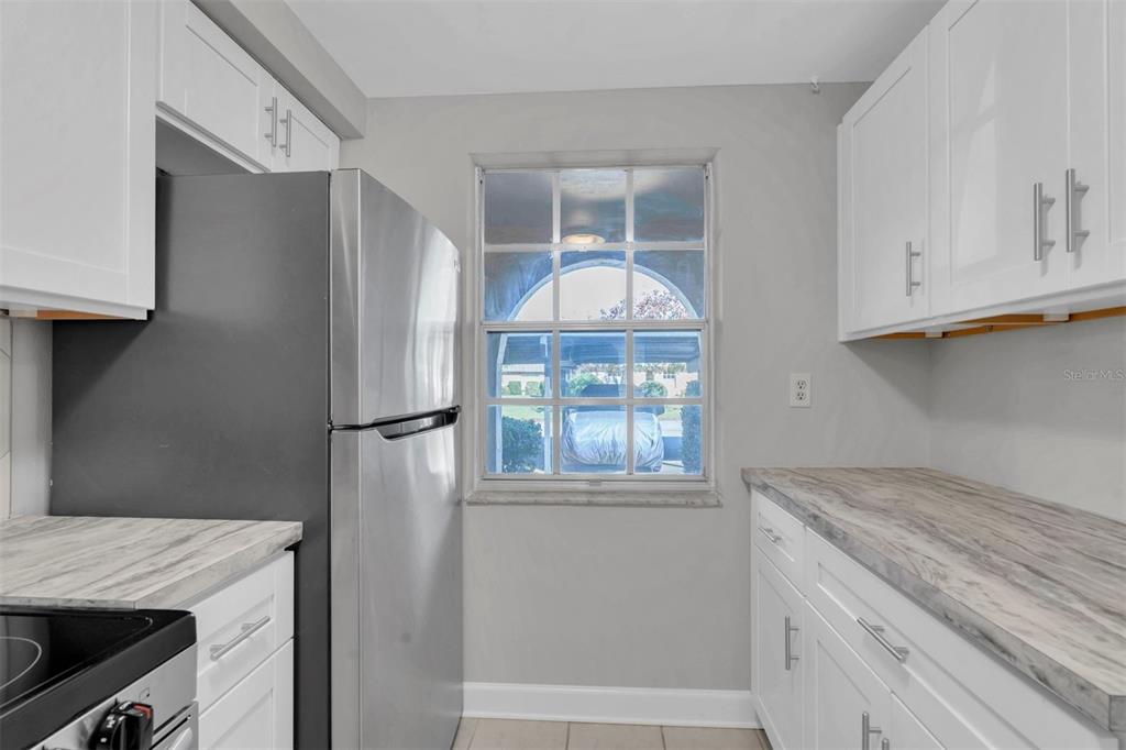 A kitchen features white cabinets, a stainless steel refrigerator, and a window overlooking a driveway — 4343 SUMMERSUN DRIVE UNIT 4343, NEW PORT RICHEY, FL