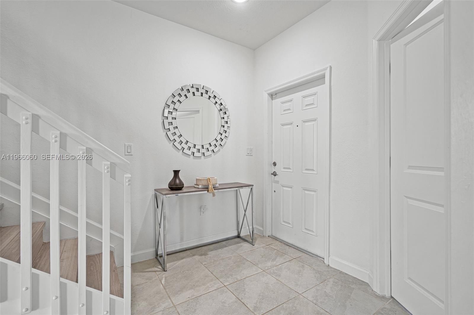 This entryway features a white door, a console table, a round mirror, and a staircase — 9941 SW 231st Ln # 9941, Miami FL 33190, MIAMI, FL