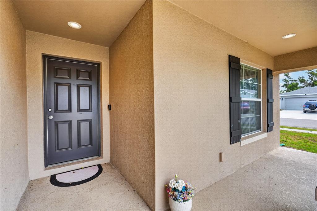 A covered entryway features a dark front door, a window with shutters, and stucco walls — 243 SANDESTIN DRIVE, HAINES CITY, FL