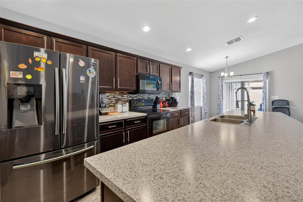 A kitchen features dark wood cabinets, stainless steel appliances, and a large speckled island countertop — 243 SANDESTIN DRIVE, HAINES CITY, FL