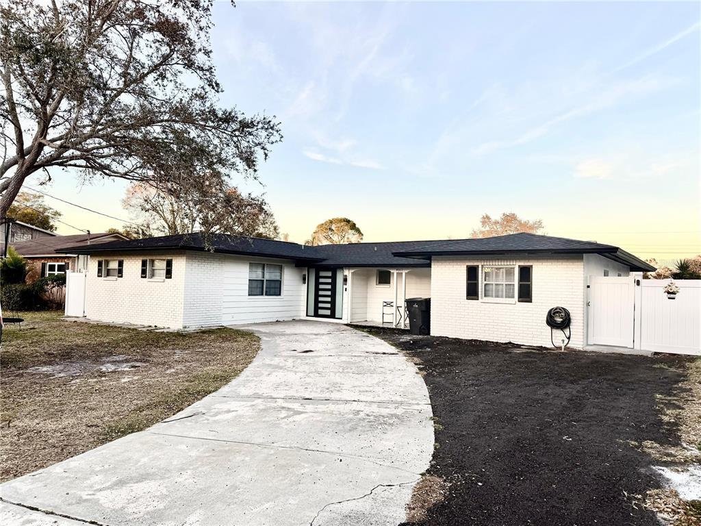 A white brick, single-story house features a black roof and a curved concrete driveway — 4911 SHETLAND AVENUE, TAMPA, FL