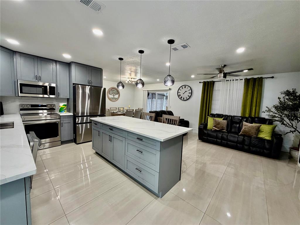 A modern kitchen with gray cabinets and a white island opens into a living area — 4911 SHETLAND AVENUE, TAMPA, FL