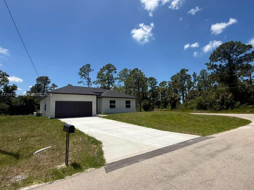A single-story house with a dark garage door and a concrete driveway under a blue sky — 908 WINTERS ST E, Lehigh Acres FL 33974, LEHIGH ACRES, FL