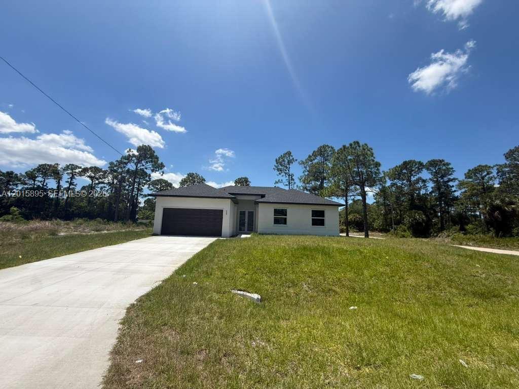 A single-story house with a garage and concrete driveway sits on a grassy lot — 908 WINTERS ST E, Lehigh Acres FL 33974, LEHIGH ACRES, FL
