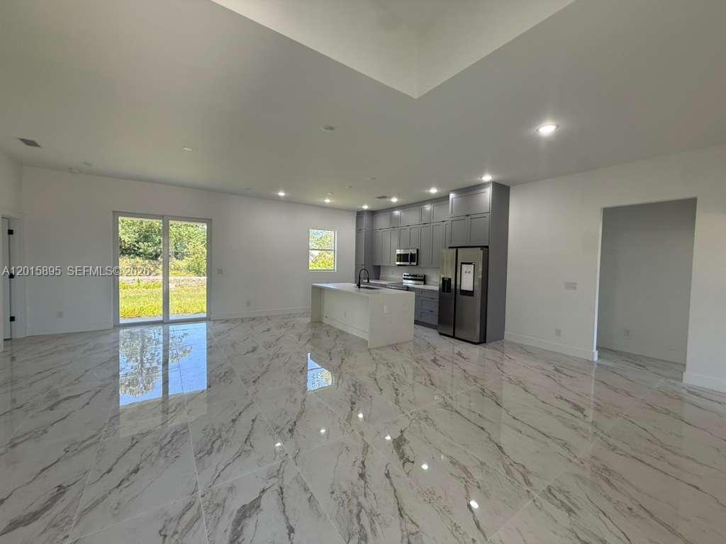 A modern kitchen with gray cabinets and a white island sits in an open-concept room — 908 WINTERS ST E, Lehigh Acres FL 33974, LEHIGH ACRES, FL