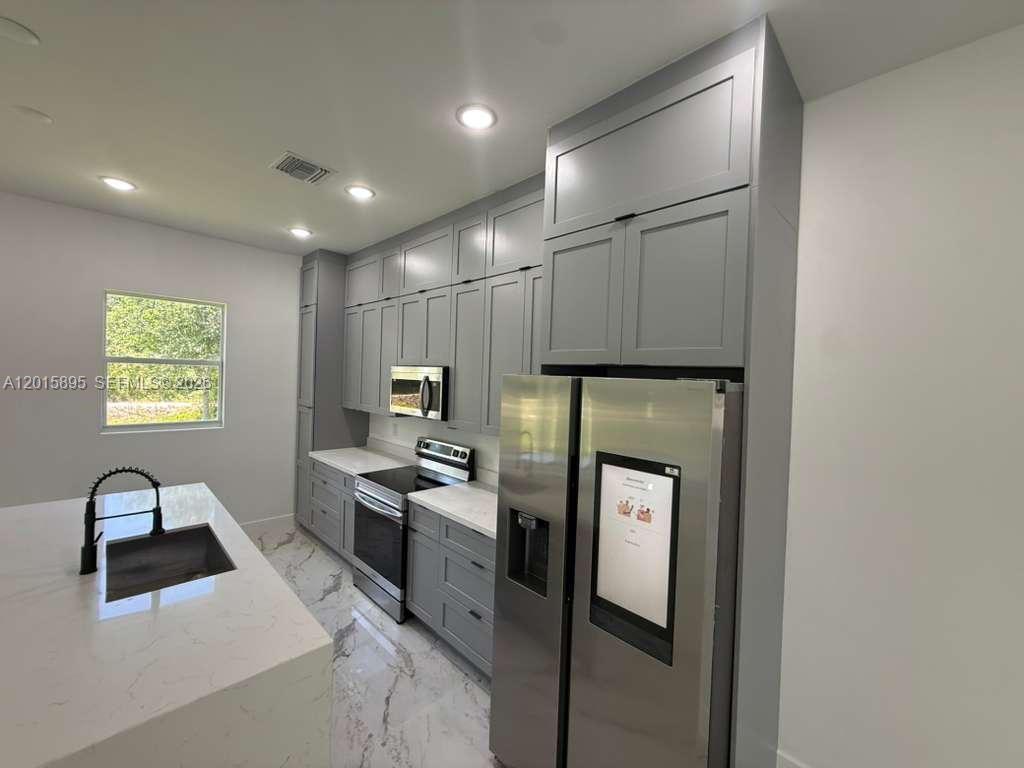 A modern kitchen features gray cabinets, stainless steel appliances, and a marble-patterned island countertop — 908 WINTERS ST E, Lehigh Acres FL 33974, LEHIGH ACRES, FL