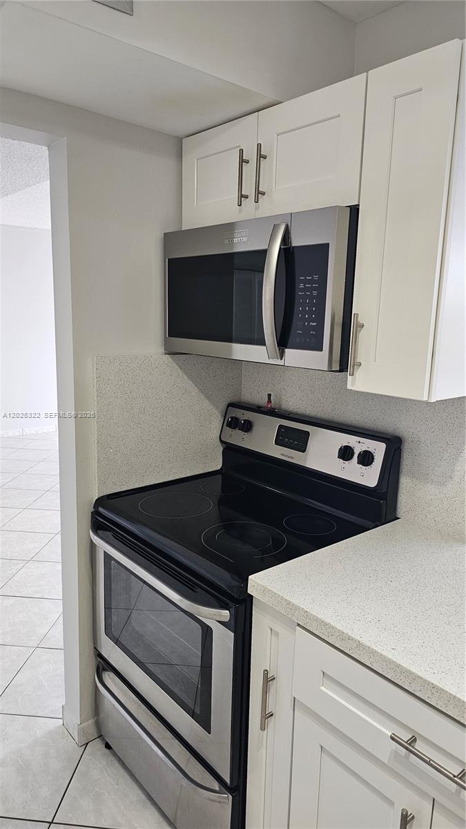 A kitchen features white cabinets, a stainless steel microwave, and a black electric range — 2017 S Ocean Dr # 408, Hallandale Beach FL 33009, HALLANDALE BEACH, FL
